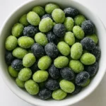 미세한 얼음 결정이 덮인 초록색 콩과 검은콩이 하얀 그릇 위에서 천천히 신선함을 유지하며 녹고 있습니다.