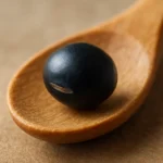 나무 숟가락 위에 놓인 검은콩 한 알의 표면 질감이 상세하게 표현되어 있습니다.