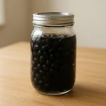 맑은 천연 식초가 채워진 유리병에 담긴 검은콩 식초 절임의 정갈한 모습입니다.