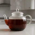 맑은 유리 다관에 담긴 따뜻하고 붉은 갈색빛의 검은콩 차가 테이블 위에 놓여 있습니다.