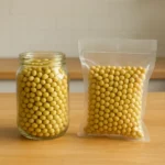 주방 조리대 위에 일반 유리병과 진공 포장지에 각각 담겨 있는 신선한 콩을 비교한 형태입니다.