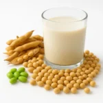 깨끗한 배경 위에 신선한 대두가 놓여 있고 건강한 단백질을 상징하는 두유 한 잔이 배치된 모습입니다.