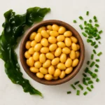 나무 그릇에 담긴 노란 콩과 주변에 놓인 신선한 다시마와 부추의 모습입니다.